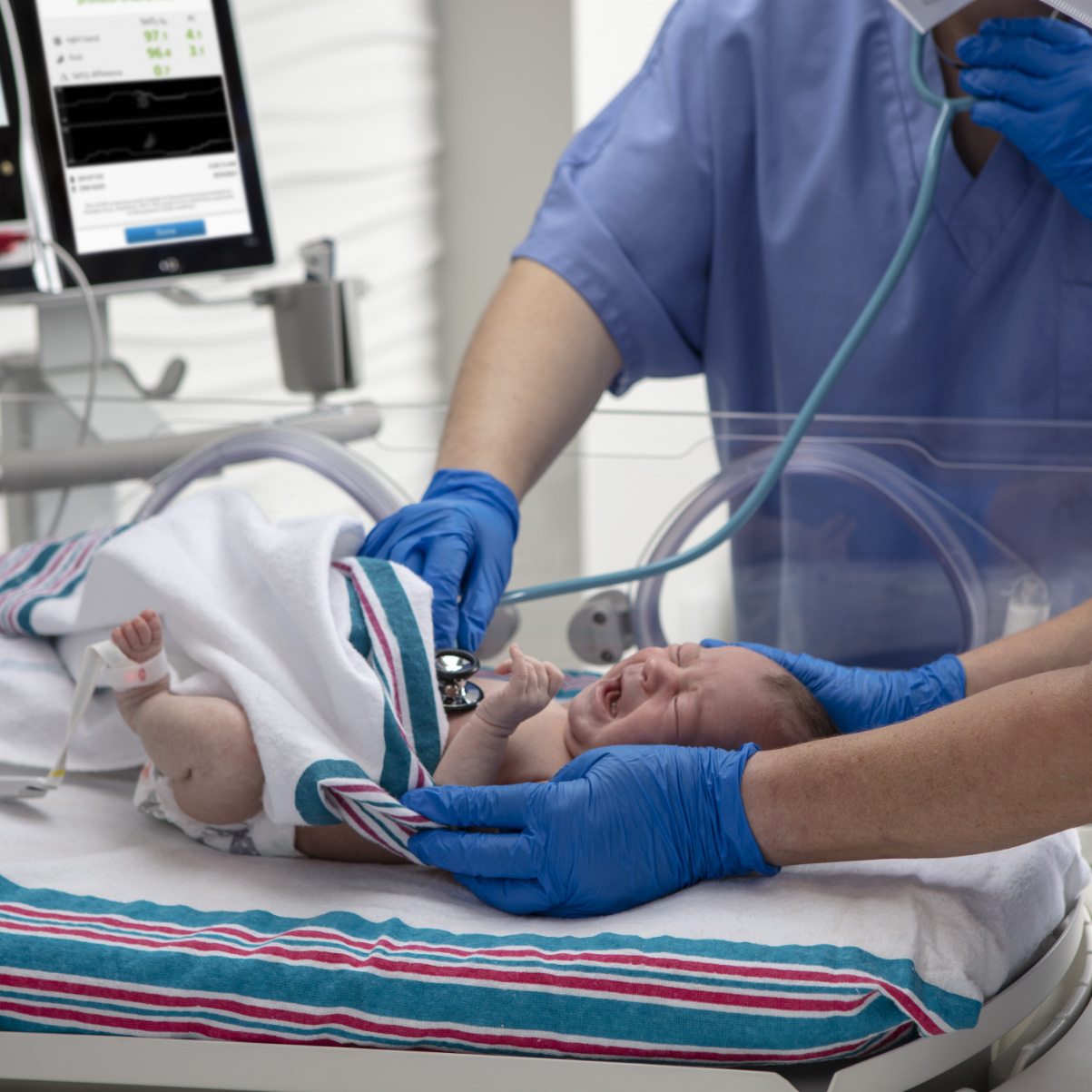 Un recién nacido examinado por los médicos con un estetoscopio y monitorizado con un sensor de oximetría de pulso Masimo Newborn.